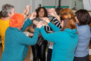 Welcome Circles participants at an event in Ireland in 2022. A group are dancing in a circle, holding raised hands together.