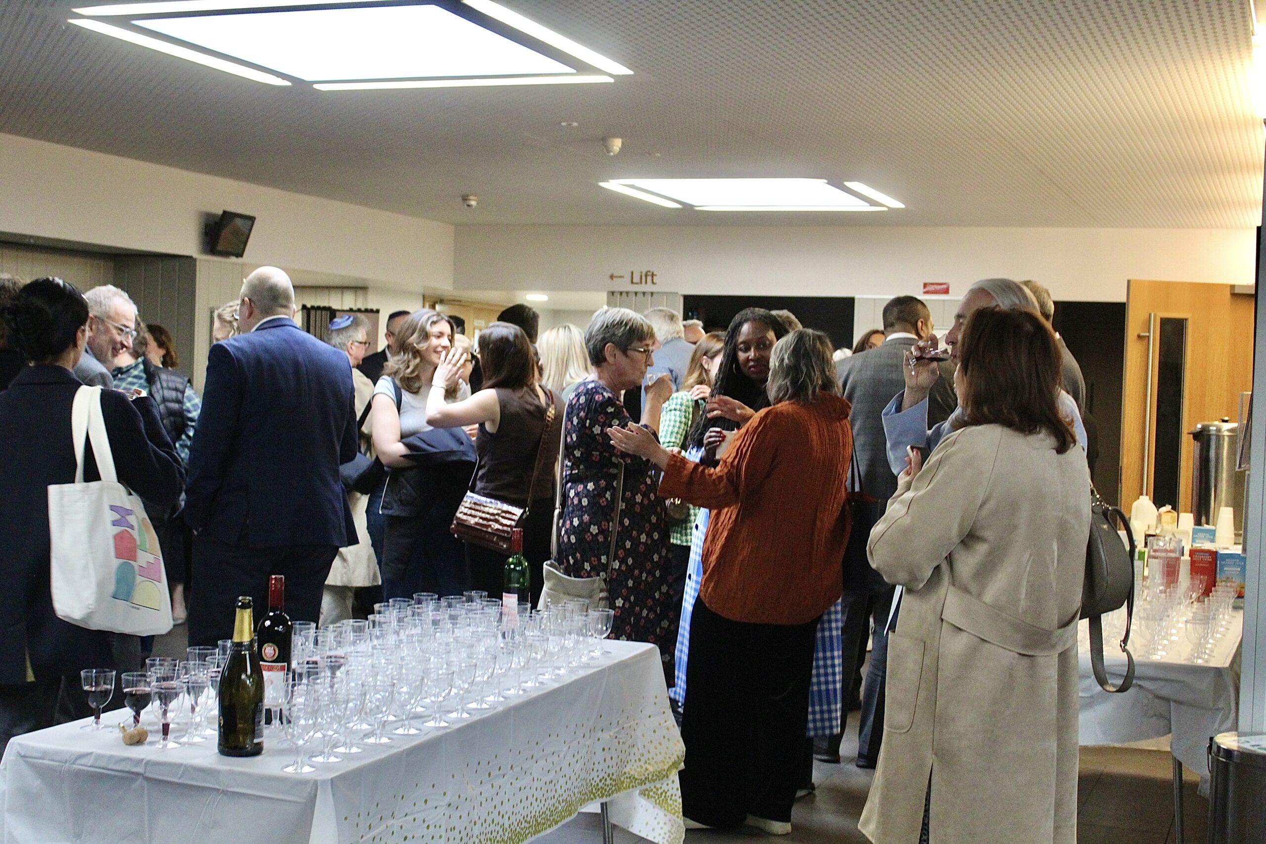 Attendees chat at the event reception. They are stood behind a table with glasses on.