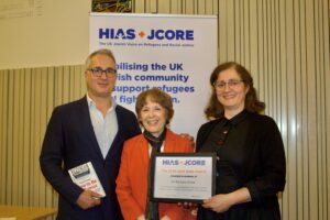 Edie Friedman (HIAS+JCORE's Executive Director) stands with Dr Richard Stone's children. They are holding the 2024 Lord Dubs Award certificate.