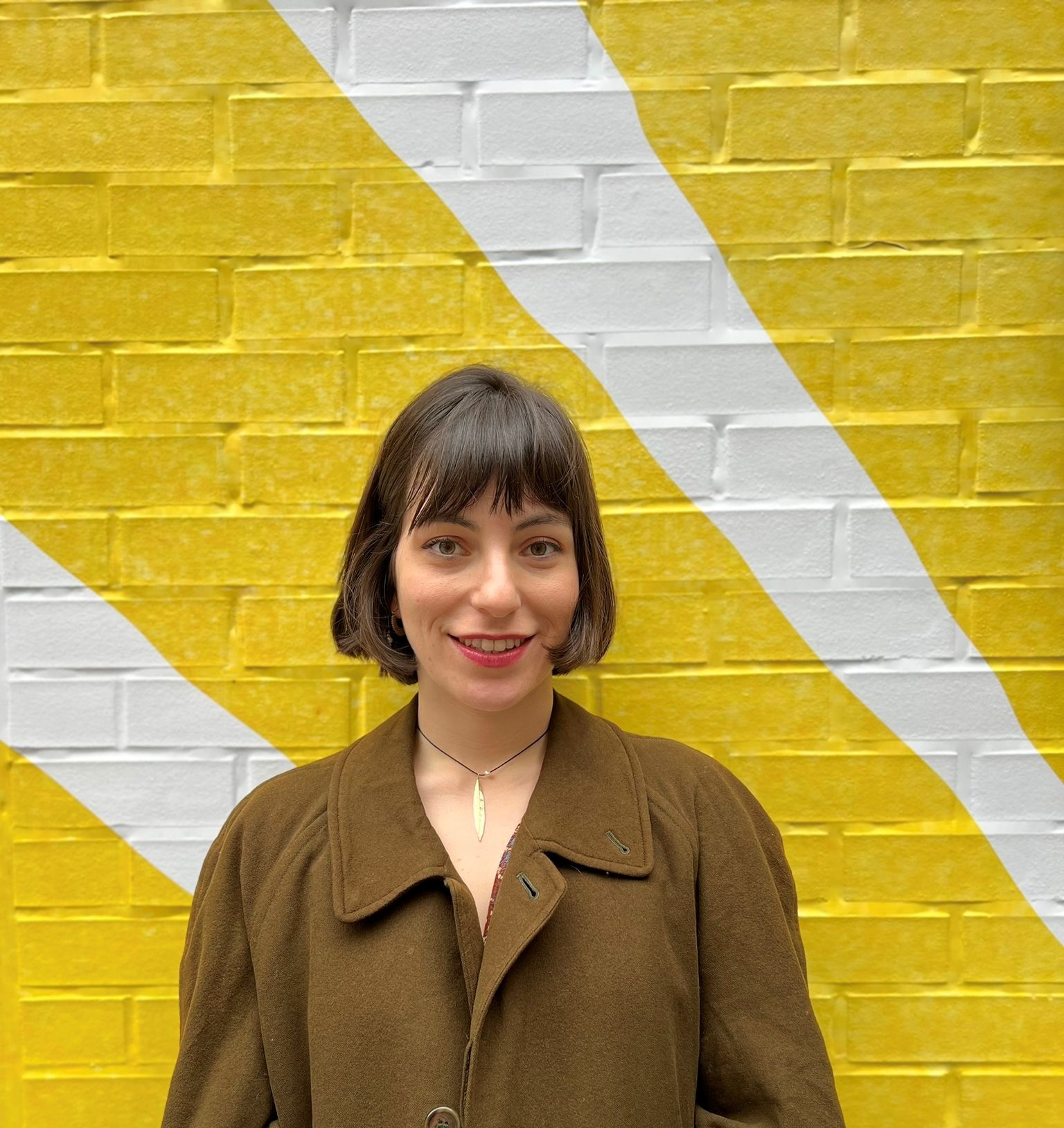 A headshot of Natalia Galgos. She is wearing a dark green shirt in front of a yellow wall.