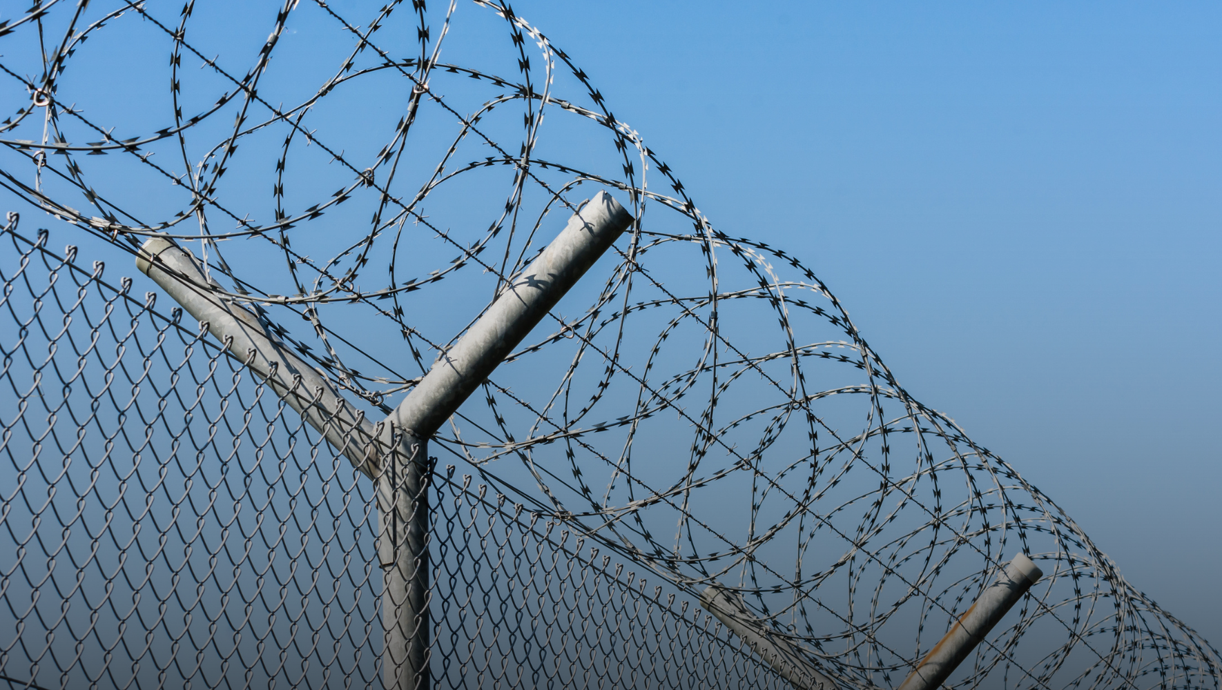 A side view of a barbed wire fence, with a sunny sky.