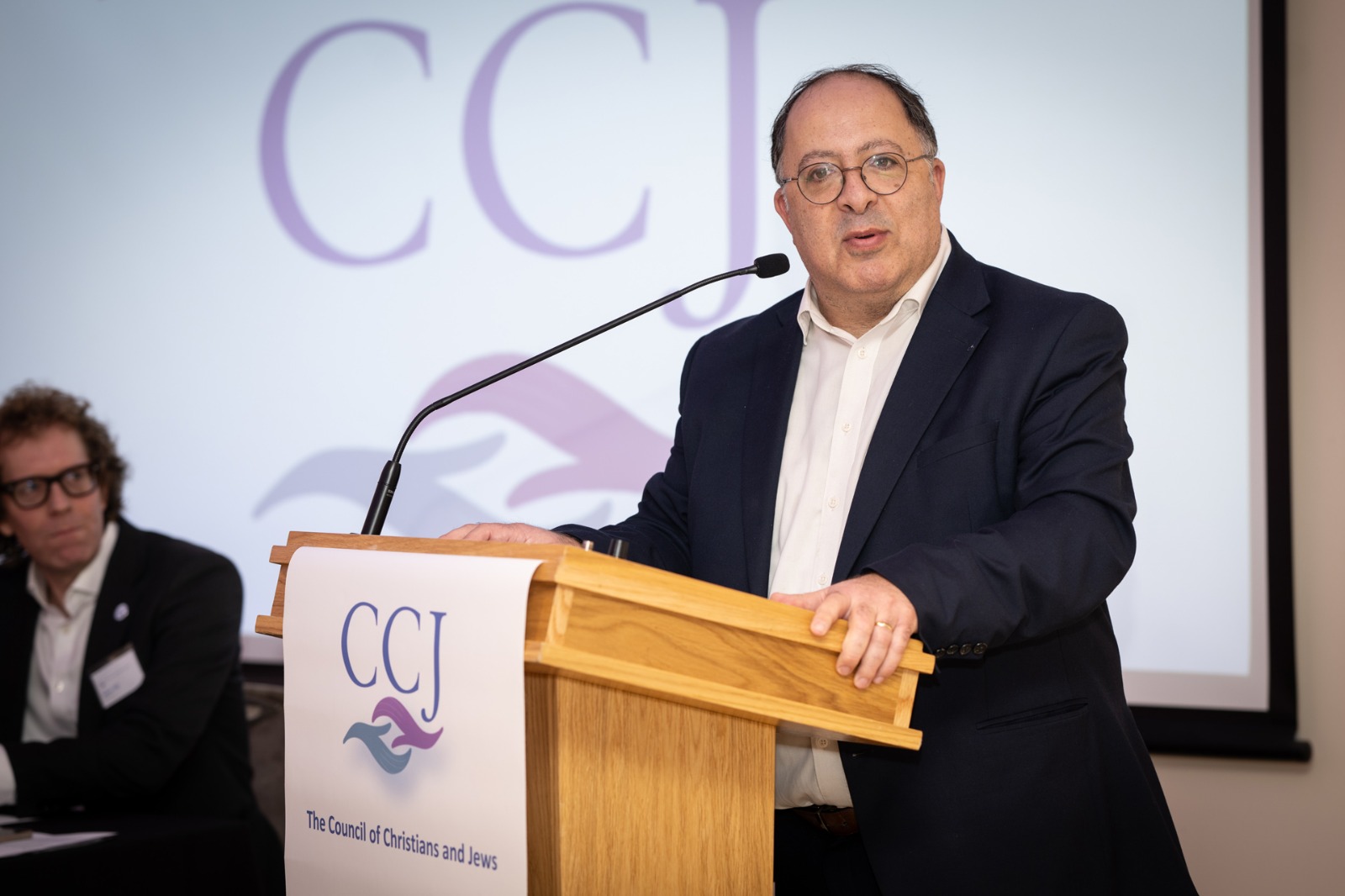 HIAS+JCORE's Executive Director Rabbi David Mason stands at a lectern at the CCJ's 2024 AGM.